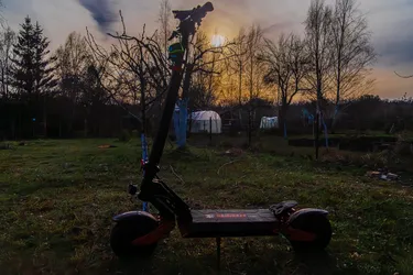 hulajnoga elektryczna Kamikaze K1 Max w ogrodowej scenerii, zdjęcie specjalnie niedoświetlone, lekko zachodzące Słońce